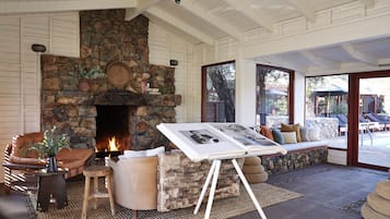 A cozy living room with a stone fireplace, comfortable seating, and a view of the outdoor pool area.