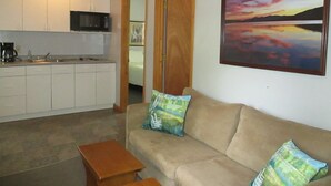 A compact living space with a kitchenette, a sofa with cushions, and a painting of a sunset. - The Blair House (Lake George)