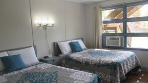 A room with two beds, each with a patterned bedspread, a nightstand with a lamp, and a window with a view of the outside. - The Blair House (Lake George)