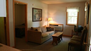 A living room with a sofa, a coffee table, a TV, and a window with curtains. - The Blair House (Lake George)
