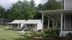A row of white cabins with a covered porch, surrounded by a well-maintained lawn and various plants. - The Blair House (Lake George)