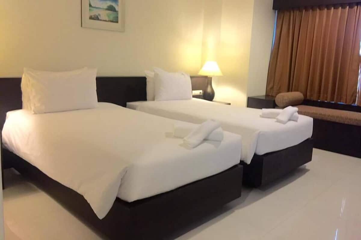 Habitación de hotel con dos camas, una mesita de noche, una lámpara, un cuadro en la pared y un ventanal con cortinas.