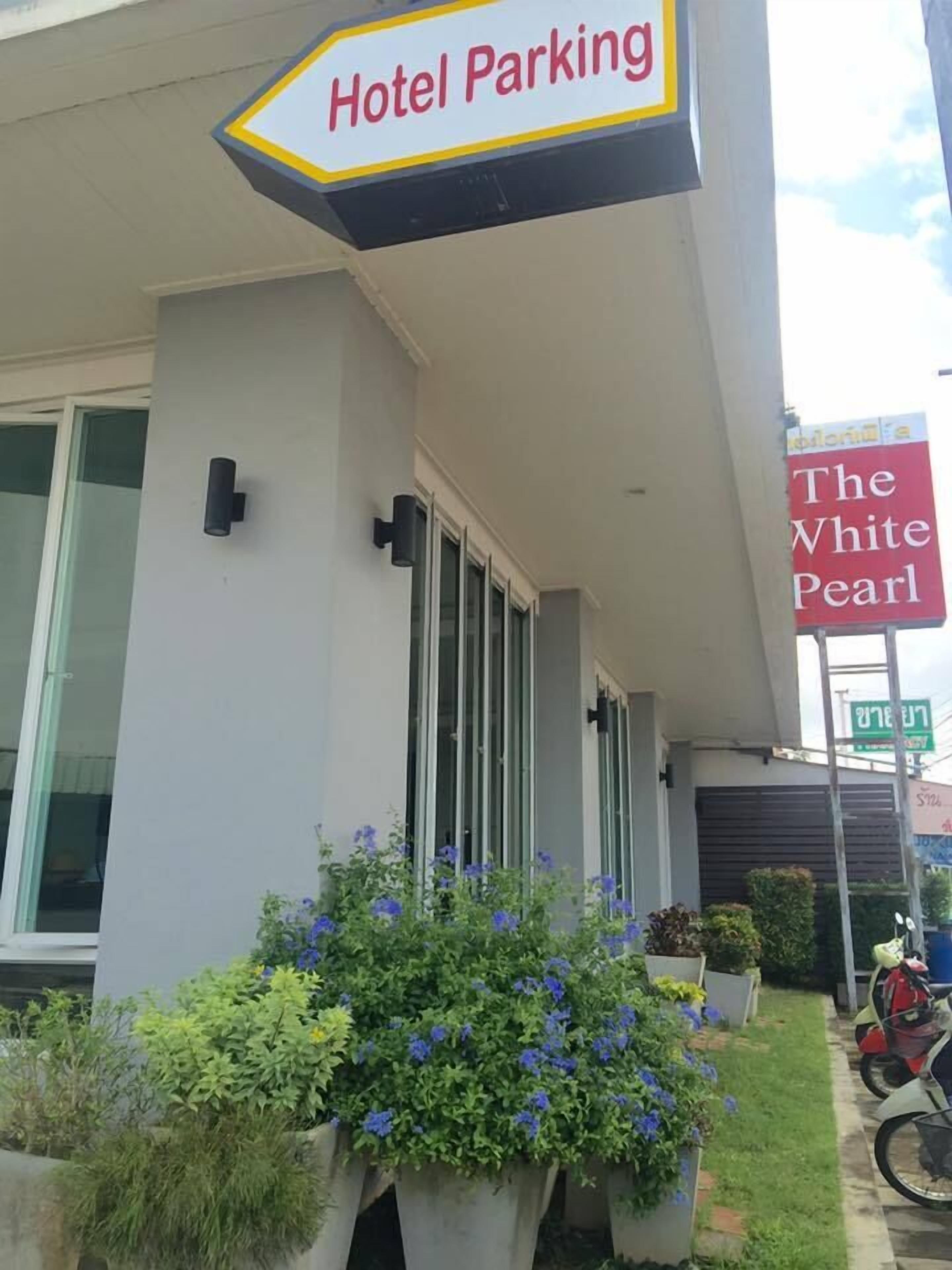 Un hotel con un letrero que dice 'Hotel Parking', un letrero que dice 'The White Pearl' y plantas en macetas al frente.