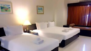 Hotellihuone, jossa on kaksi sänkyä, yöpöytä lampun kanssa ja ikkuna, jossa on verhot.