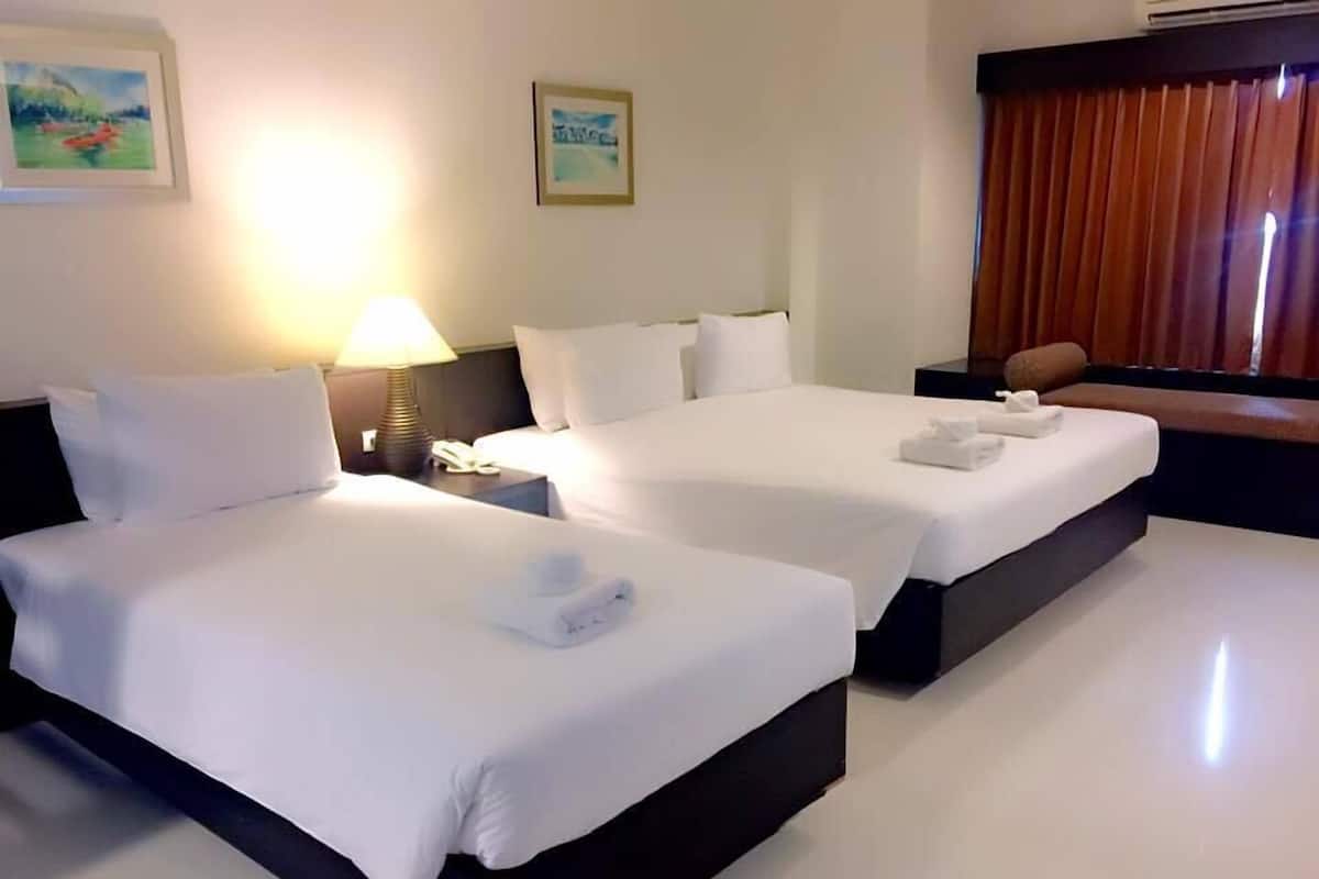 Habitación de hotel con dos camas, una mesita de noche con lámpara y una ventana con cortinas.