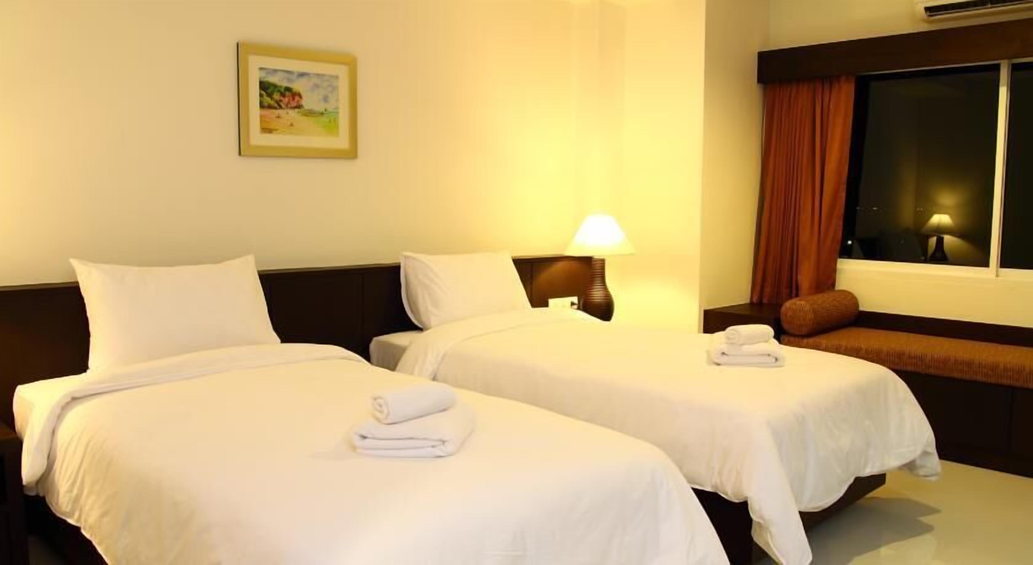 A hotel room with two beds, a nightstand with a lamp, a window with curtains, and a painting on the wall.