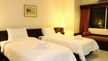 A hotel room with two beds, a nightstand with a lamp, a window with curtains, and a painting on the wall.