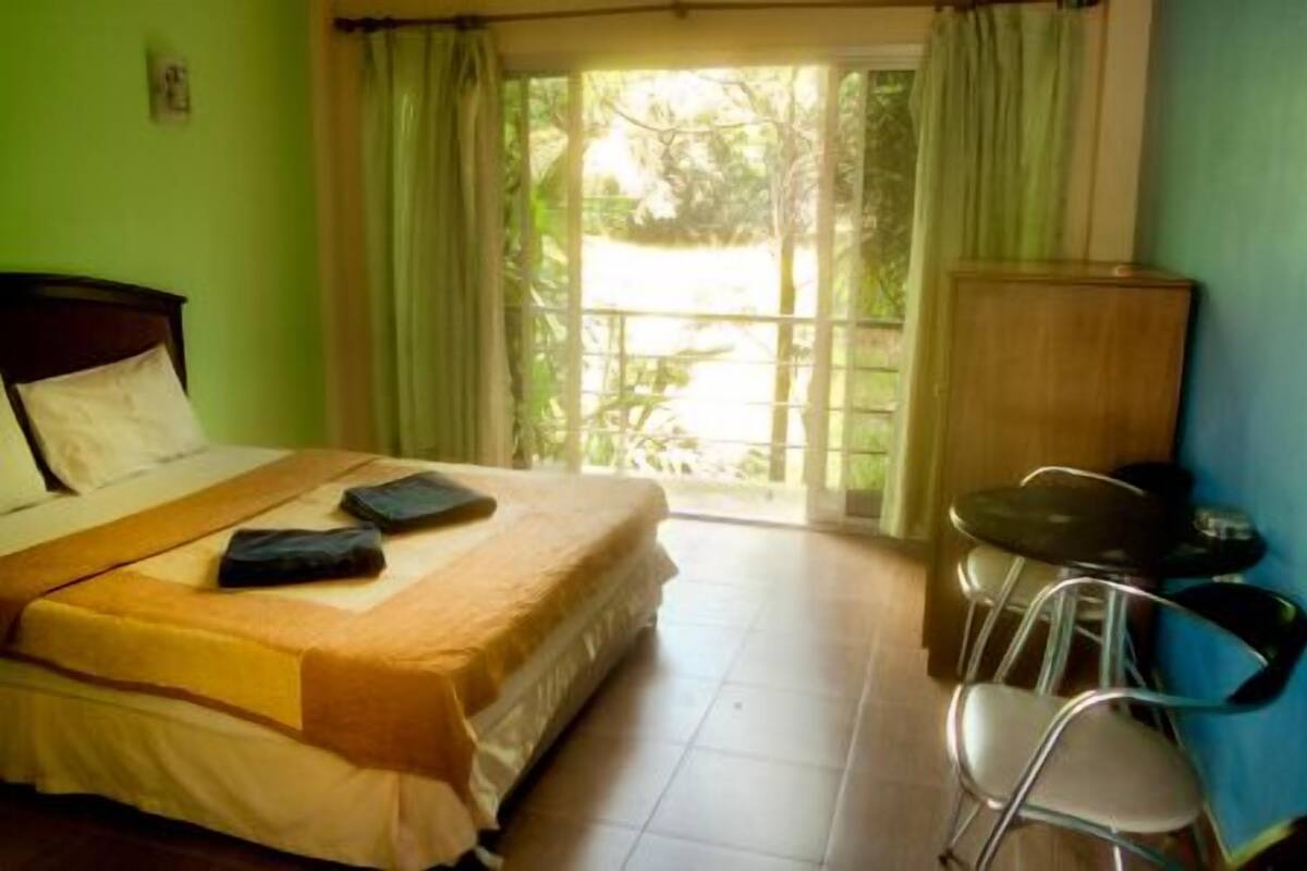 A room with a bed, a small table, a chair, and a view of the outdoors through a window.