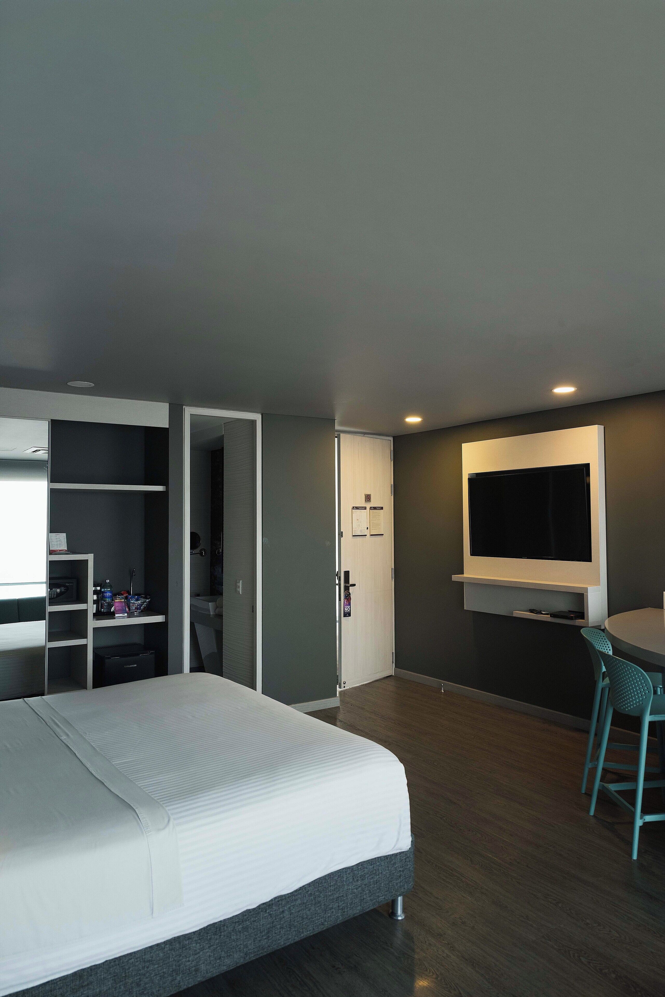 A modern hotel room with a bed, a desk with a chair, a TV mounted on the wall, and a walk-in closet.