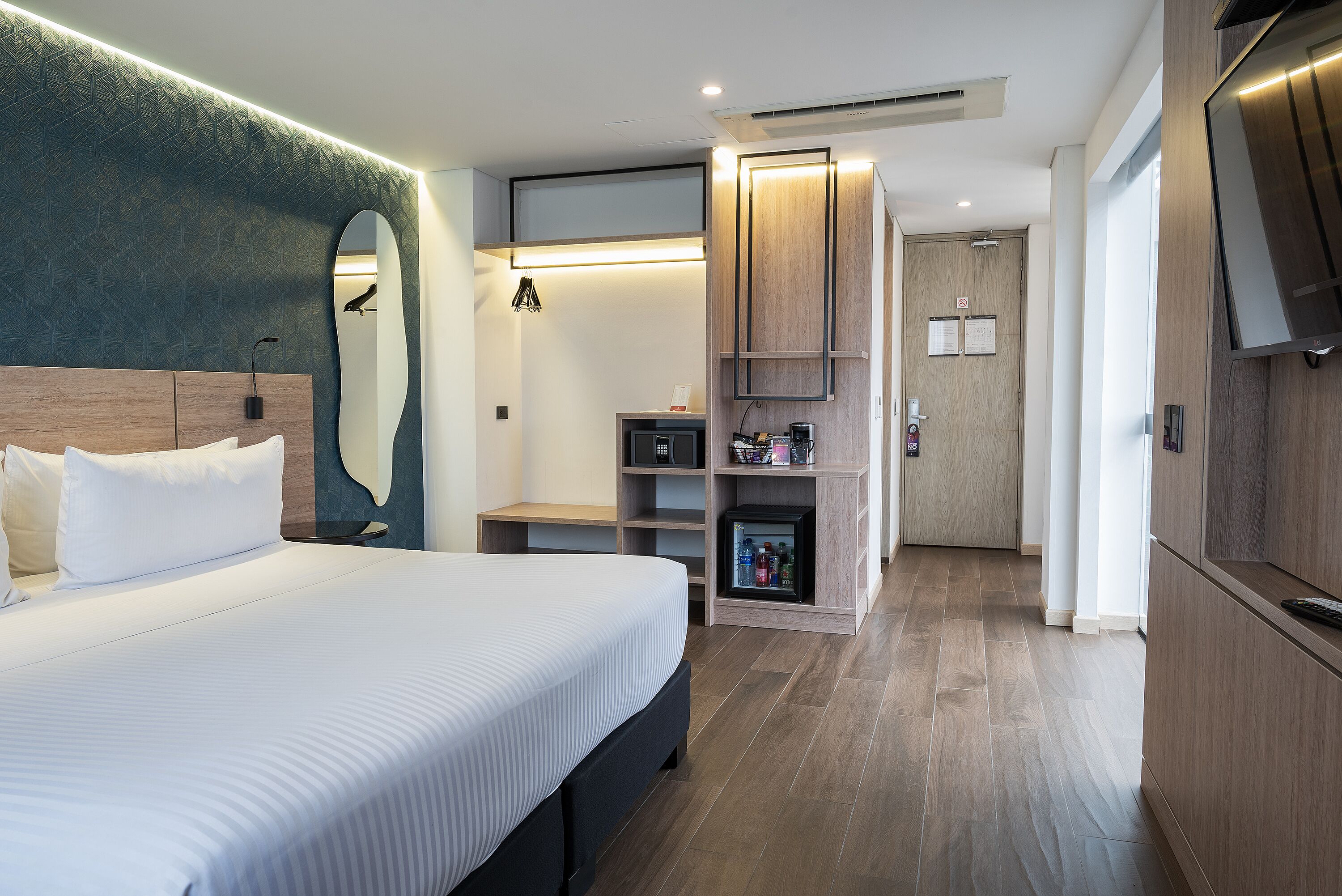 Una habitación de hotel moderna con una cama grande, un escritorio integrado, un minibar y un televisor.