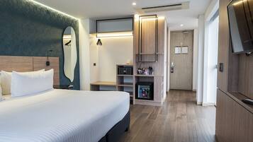 Una habitación de hotel moderna con una cama grande, un escritorio integrado, un minibar y un televisor.