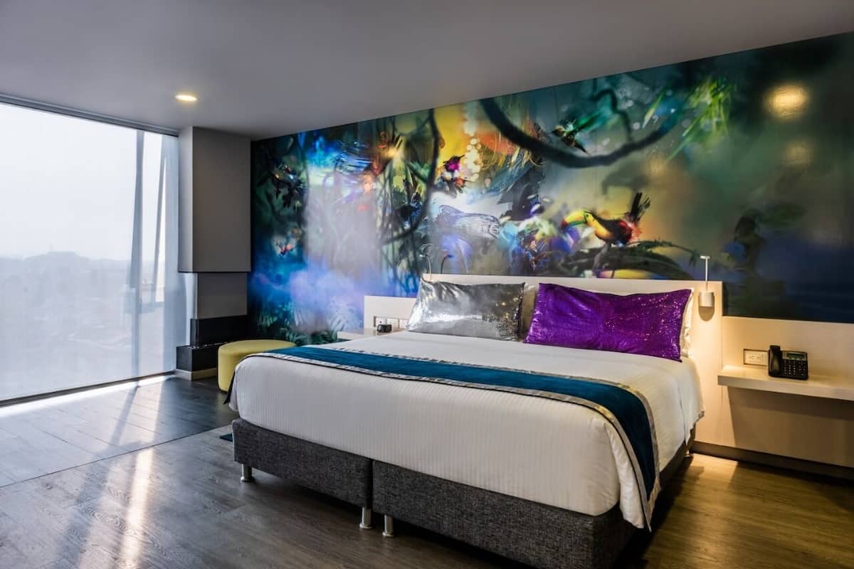 Habitación de hotel moderna con una cama grande, vistas a la ciudad y un cuadro abstracto vibrante en la pared.