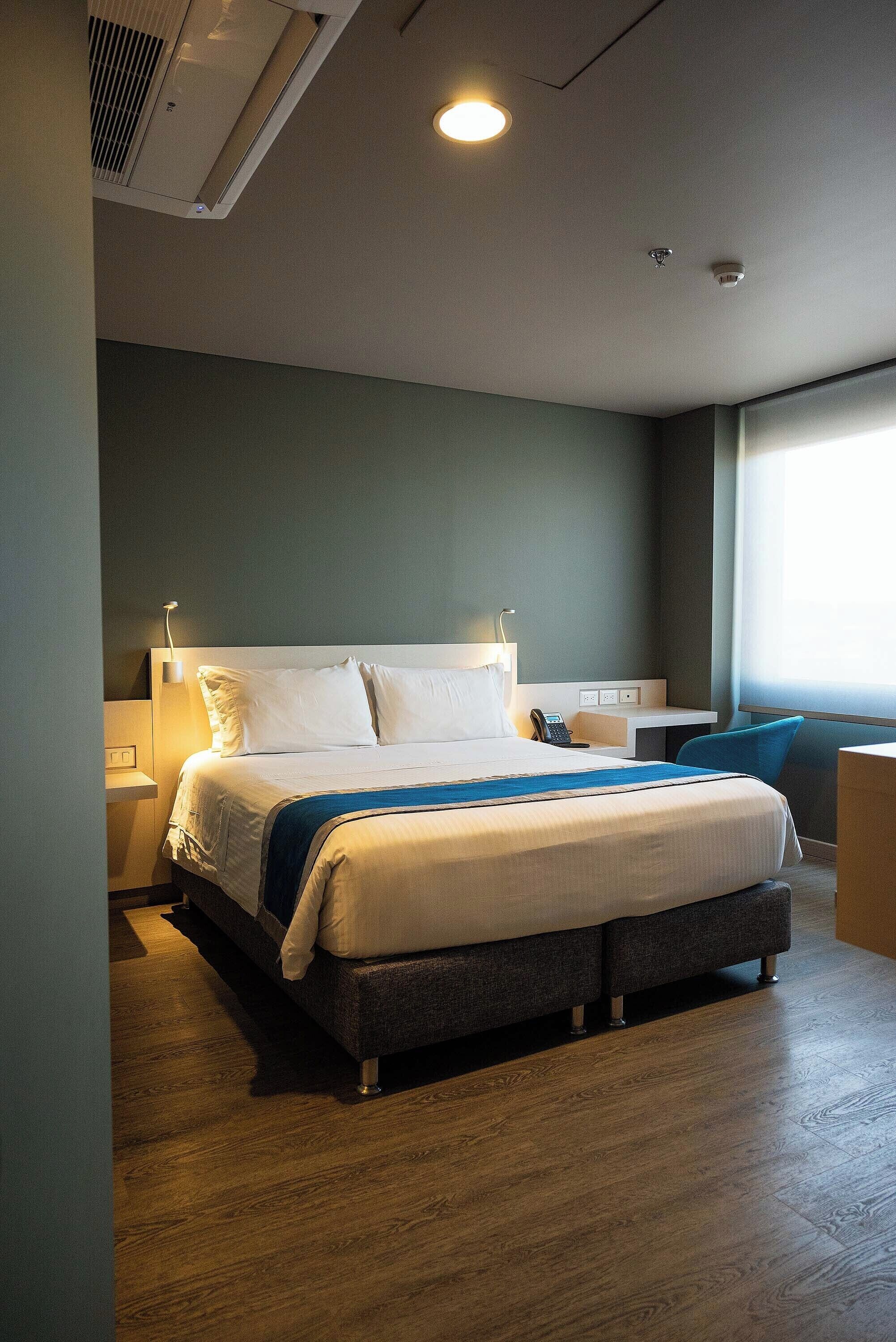 Una habitación de hotel con una cama grande, mesitas de noche, un escritorio y una ventana.