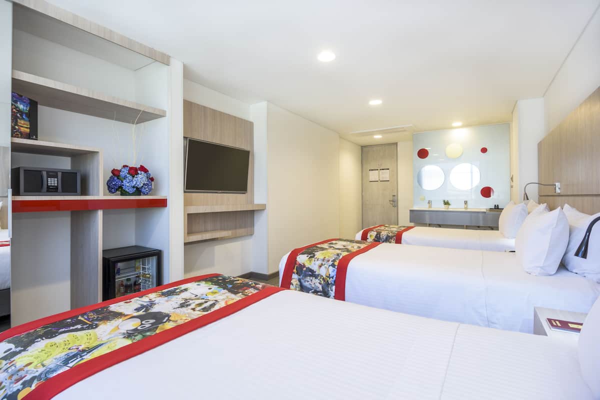 Habitación de hotel con dos camas, televisión, minibar y baño con espejo y lavamanos.