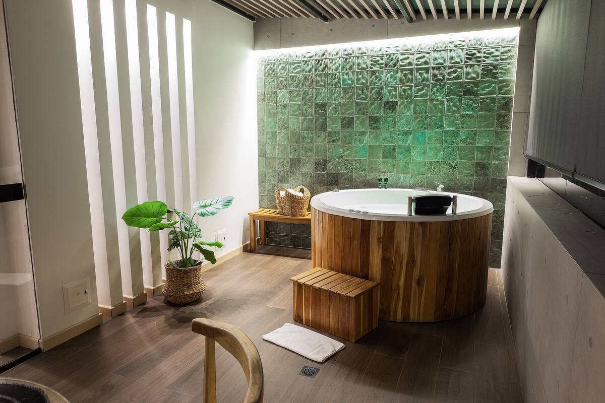 Un baño moderno con una bañera de madera, una pared de mosaicos verdes y una planta en maceta.