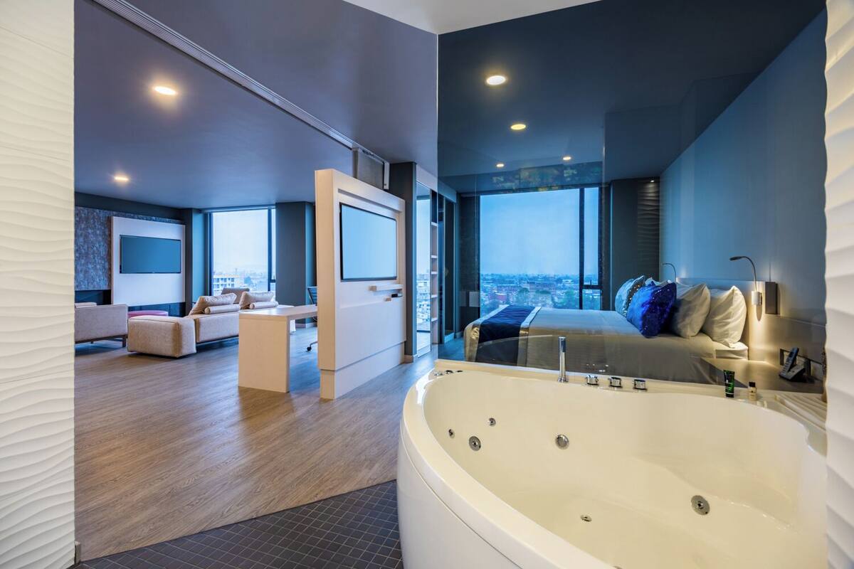 Una habitación de hotel moderna con una bañera grande, un conjunto de sofás, un televisor y vistas a la ciudad.
