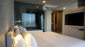 Habitación de hotel moderna con una cama grande, un televisor montado en la pared y vistas a la ciudad a través de la ventana.
