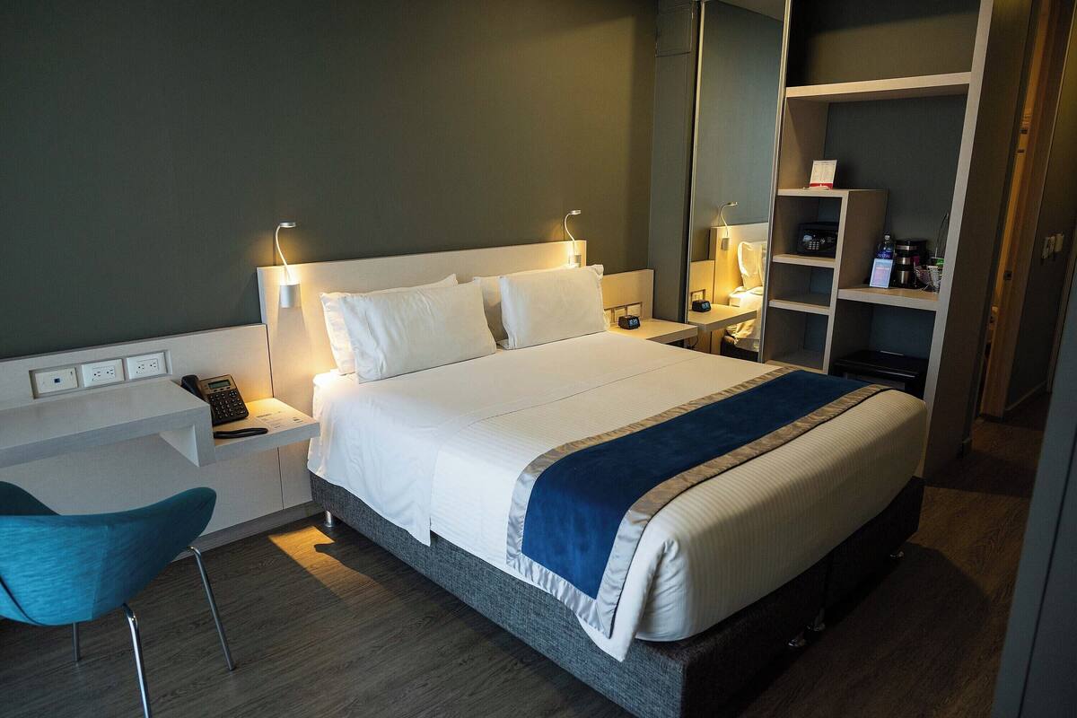 Una habitación de hotel con cama, mesitas de noche, escritorio, silla y armario.