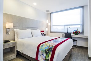 Une chambre d’hôtel moderne avec un grand lit, une table de chevet, une lampe et une fenêtre donnant sur un beau paysage.