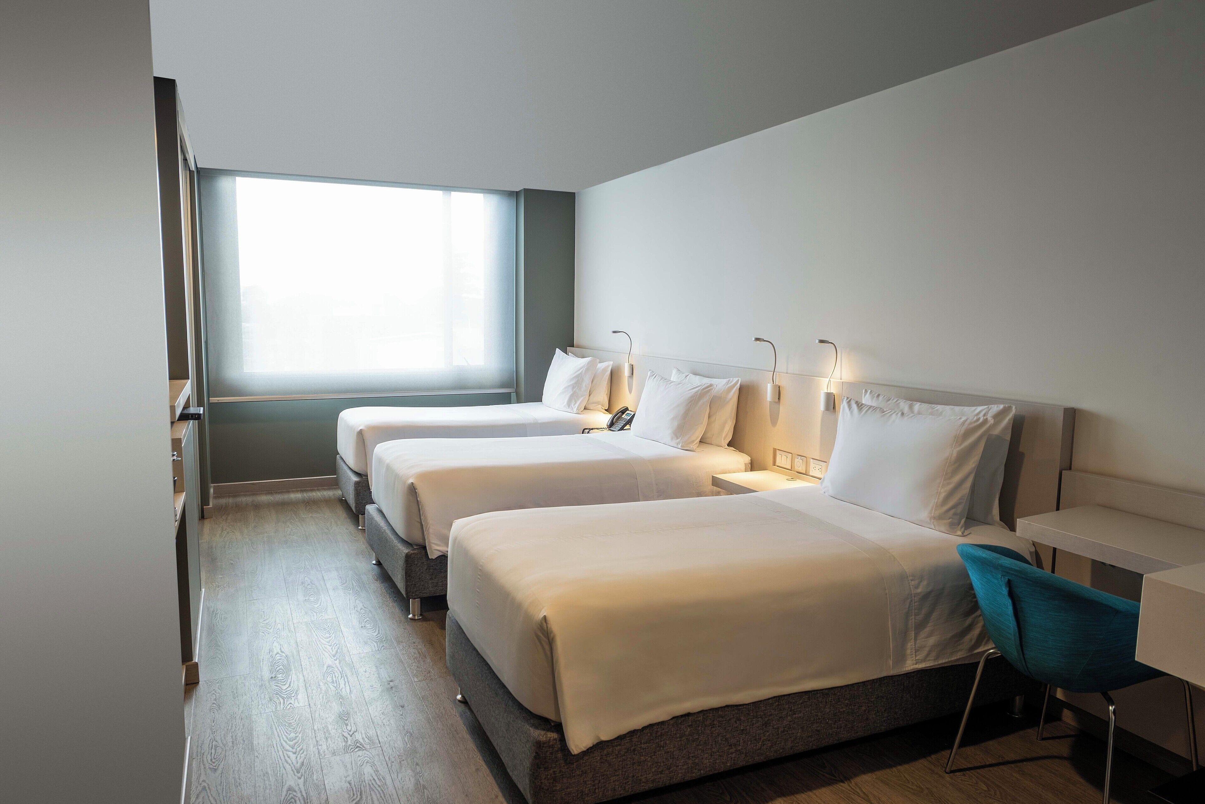 Une chambre d’hôtel avec deux lits, un bureau, une chaise et une grande fenêtre.