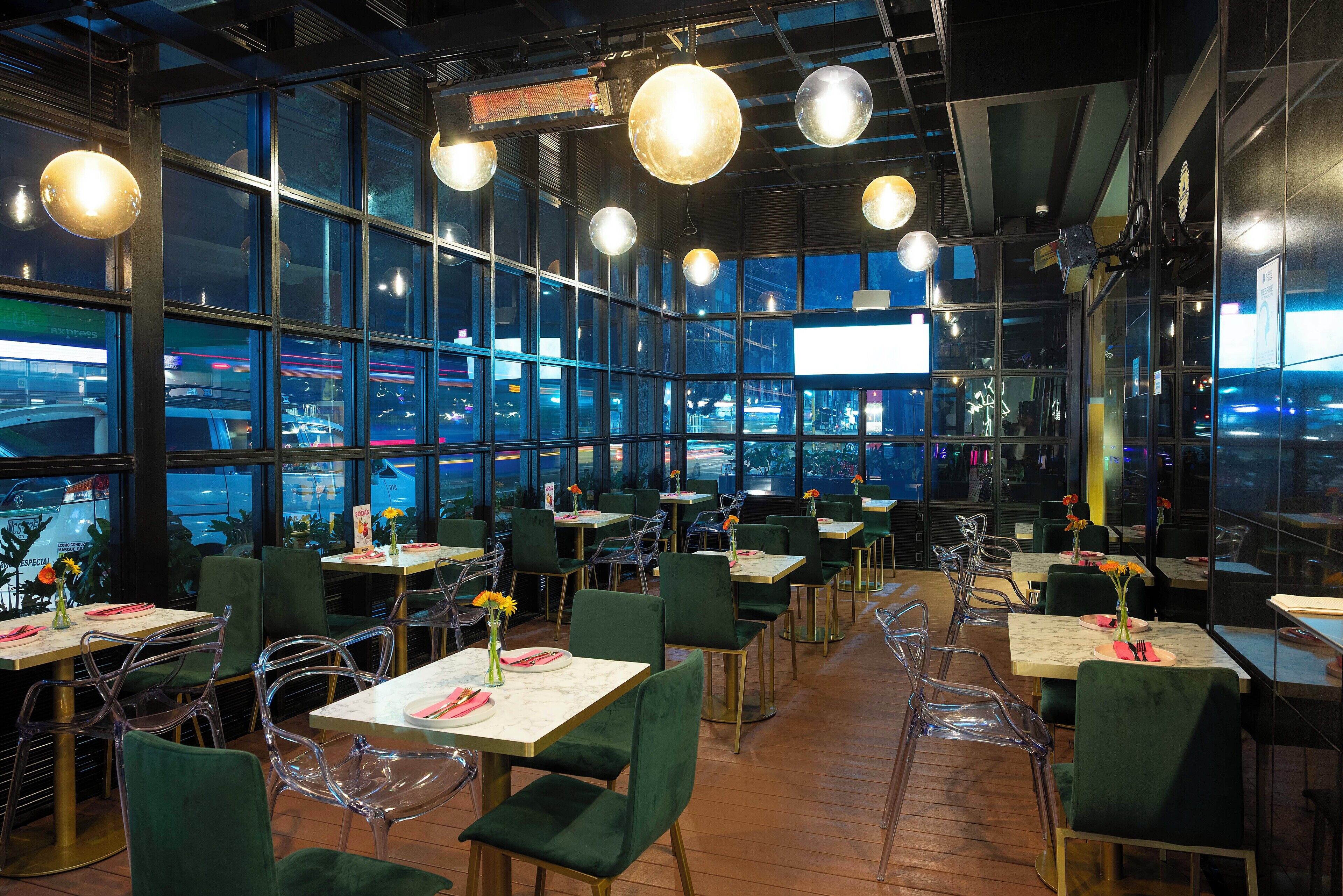 Un restaurant doté de grandes fenêtres, de chaises vertes et de tables ornées de compositions florales.
