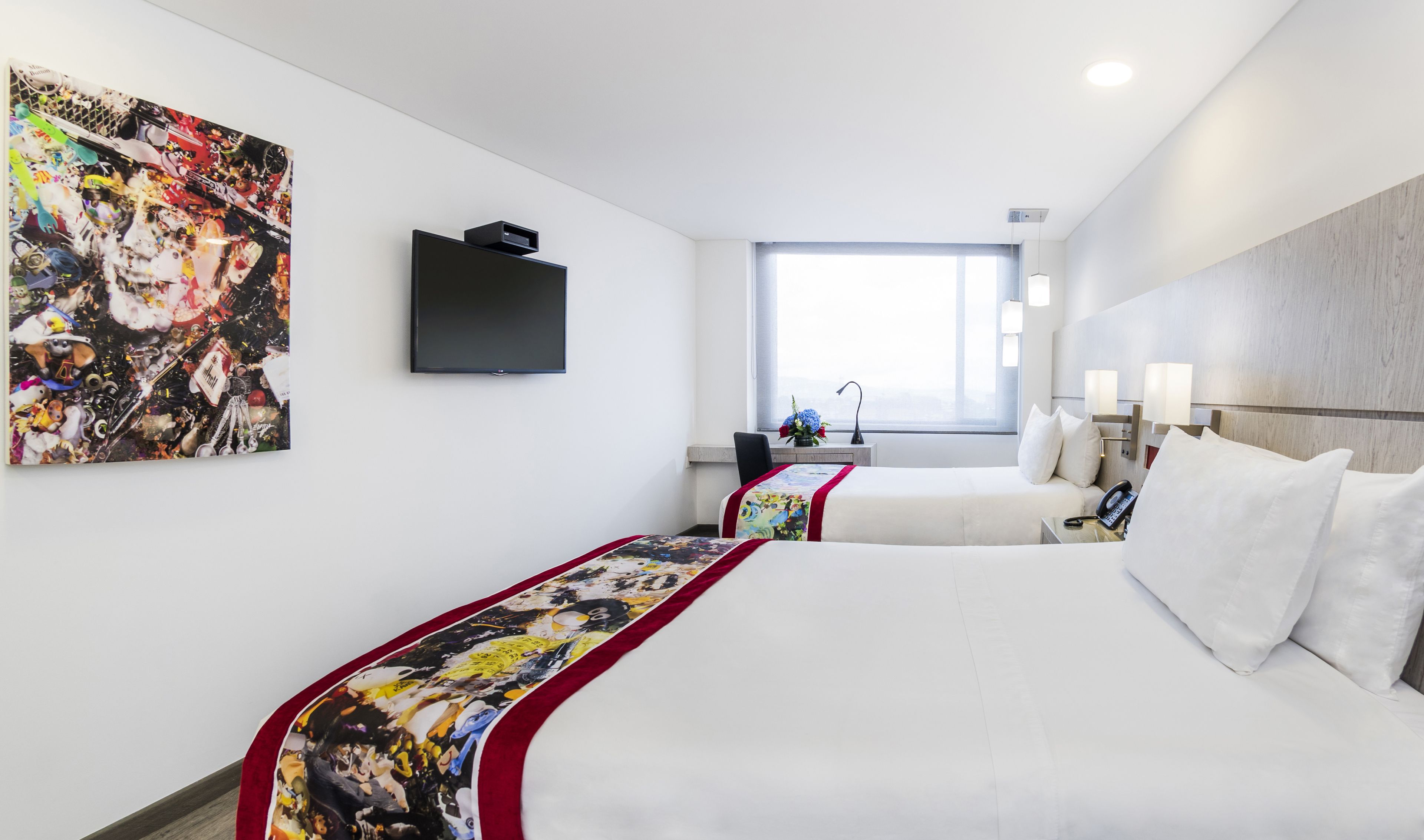Habitación de hotel con dos camas, televisión, ventana con vistas y un cuadro en la pared.