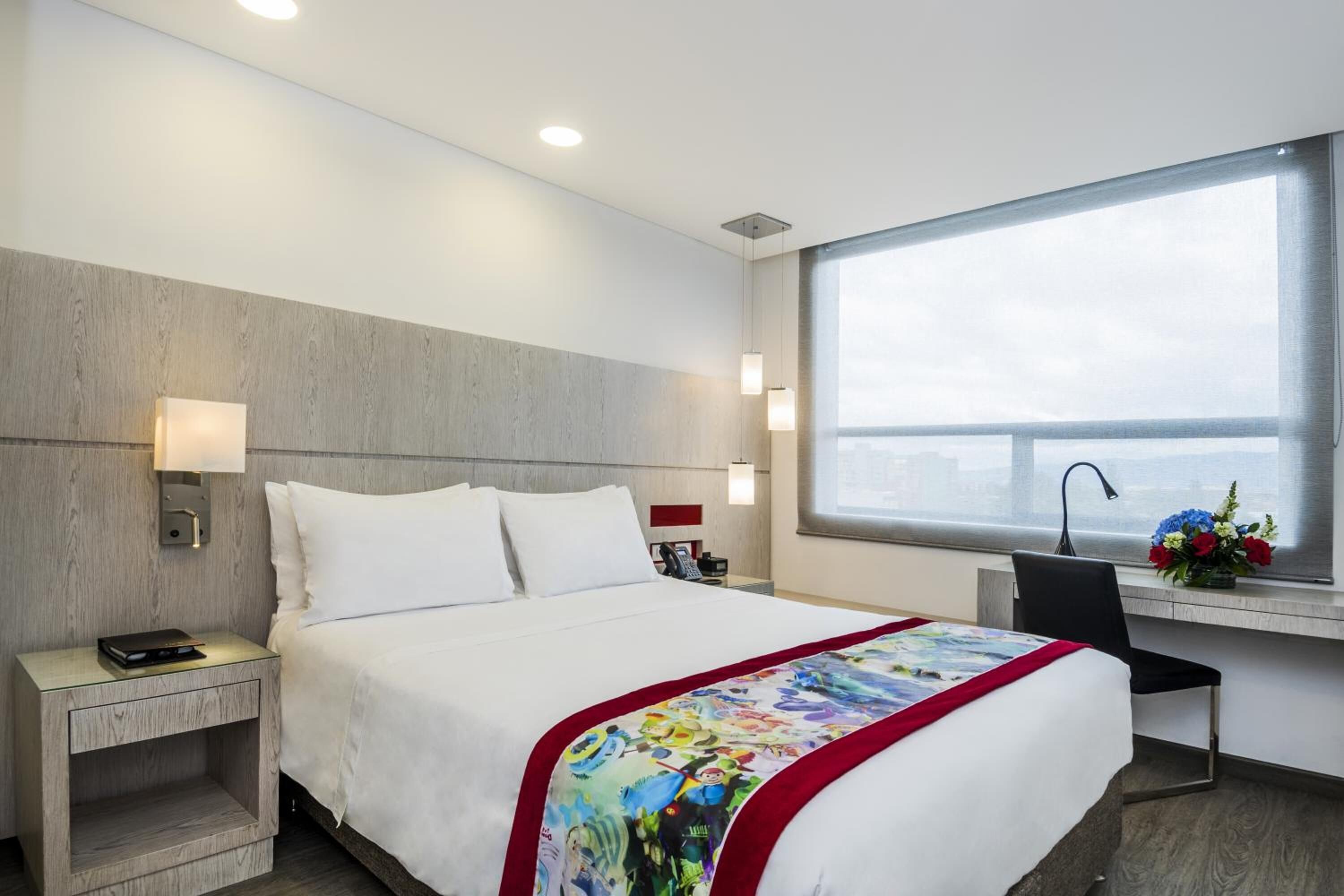 Una habitación de hotel con cama, mesita de noche, lámpara y un escritorio con silla.