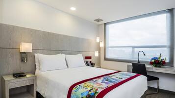 Una habitación de hotel con cama, mesita de noche, lámpara y un escritorio con silla.