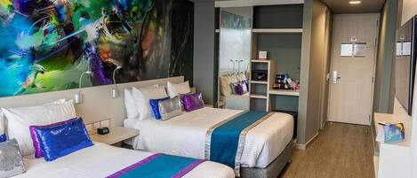 Ein Hotelzimmer mit zwei Betten, einem großen, abstrakten Gemälde an der Wand, Holzboden und einer kleinen Sitzecke mit Tisch und Stühlen.