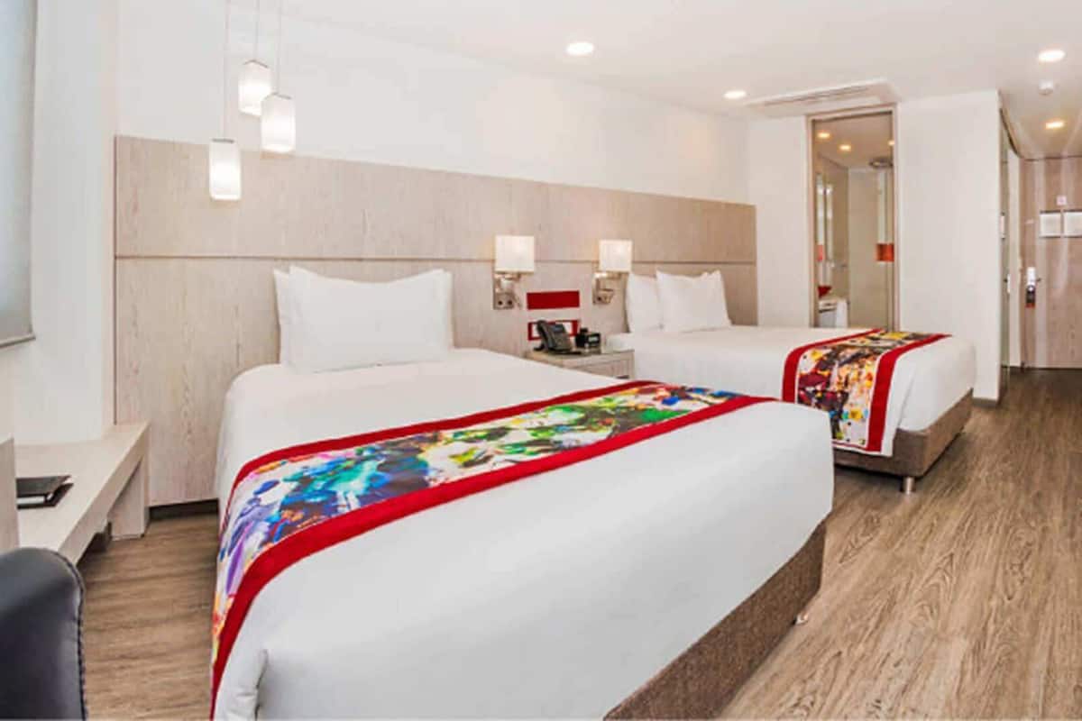 Una habitación de hotel con dos camas, un escritorio, una silla y un espejo.