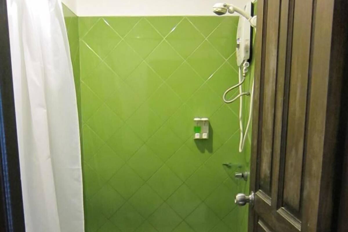 Une salle de bain avec un mur recouvert de carreaux verts, des toilettes blanches et une porte en bois.