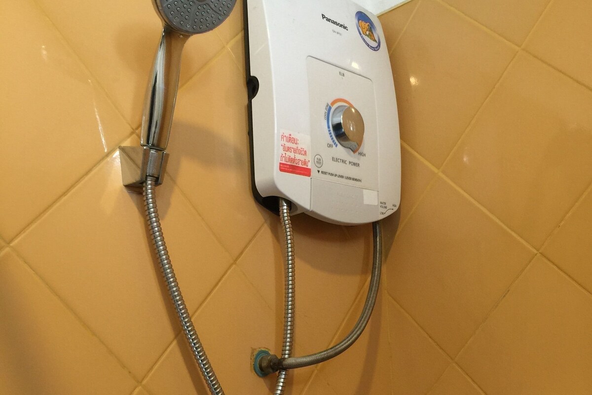 Un baño con ducha, panel de control en la pared y pared con azulejos.