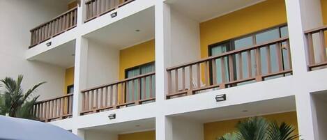 A multi-story hotel with balconies, a swimming pool, and tropical plants.