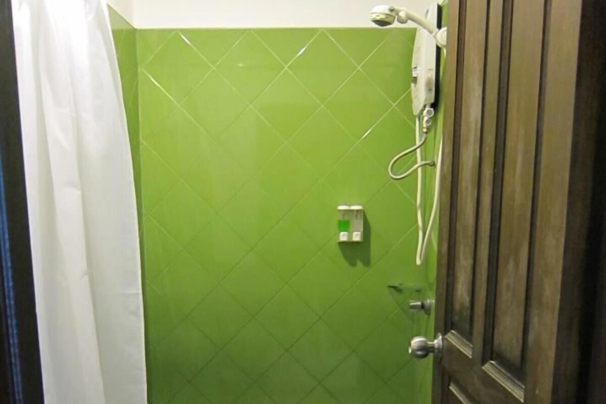 Un baño con pared de azulejos verdes, un inodoro blanco y una puerta de madera.