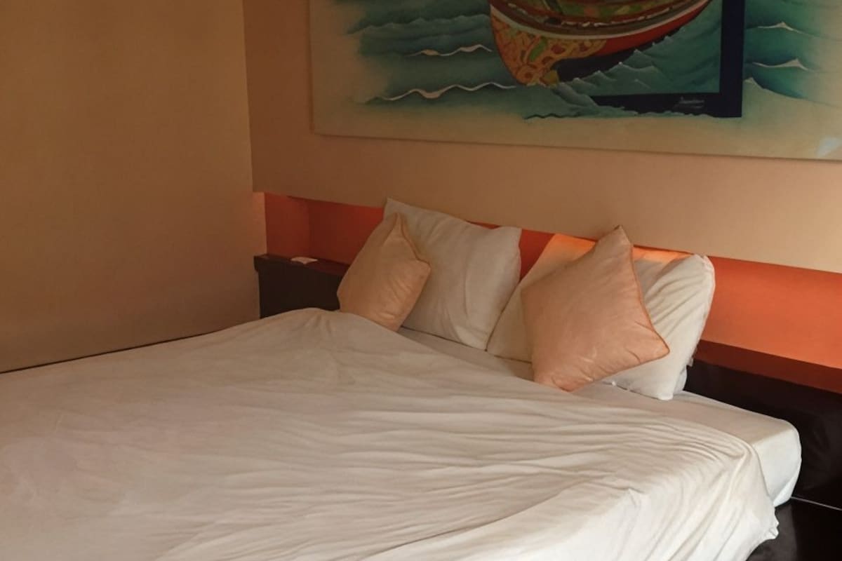 Een hotelkamer met een groot bed, een hoofdeinde met een rode accentkleur en een schilderij van een boot aan de muur.