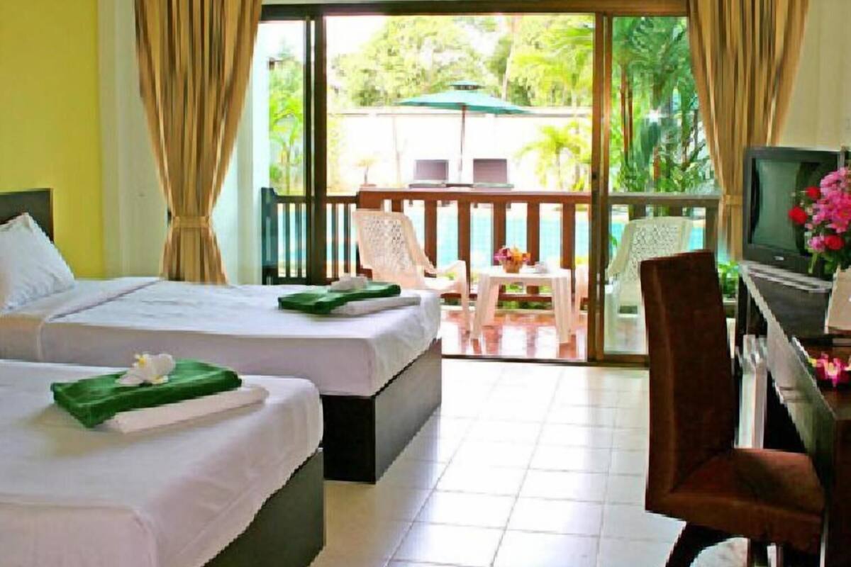 Une chambre d’hôtel avec deux lits, un bureau avec une télévision et un balcon équipé d’une table et de chaises.