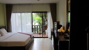 Habitación de hotel con cama, escritorio con televisor y balcón con vistas a zonas verdes.