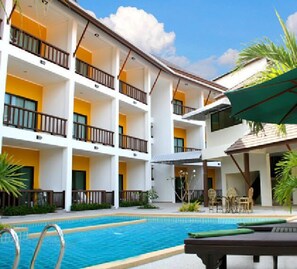 Un hotel de varios pisos con balcones, piscina y mobiliario exterior.