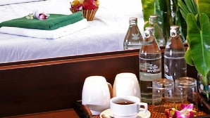 Una habitación de hotel con una cama bien hecha, una bandeja con una taza de café, un jarrón de flores y varias botellas de agua.
