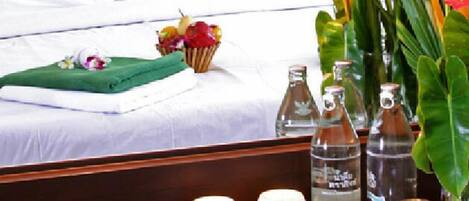 A hotel room with a neatly made bed, a tray with a cup of coffee, a vase of flowers, and several bottles of water.