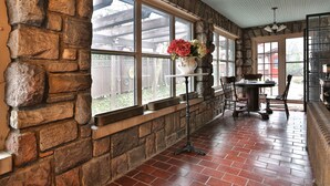 A stone-walled room with a brick floor, large windows, a table with chairs, and a vase with flowers. - Stone Chalet B&B Inn and Event Center (Ann Arbor)
