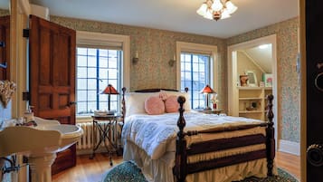 A bedroom with a wooden bed, a bedside table, a nightstand, a dresser, a mirror, and a window with a view of the outside.