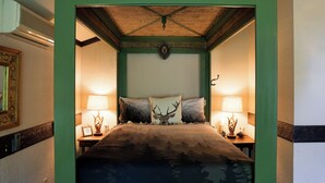 A bedroom with a bed, two lamps, a wall-mounted clock, and a decorative emblem above the bed. - Stone Chalet B&B Inn and Event Center (Ann Arbor)