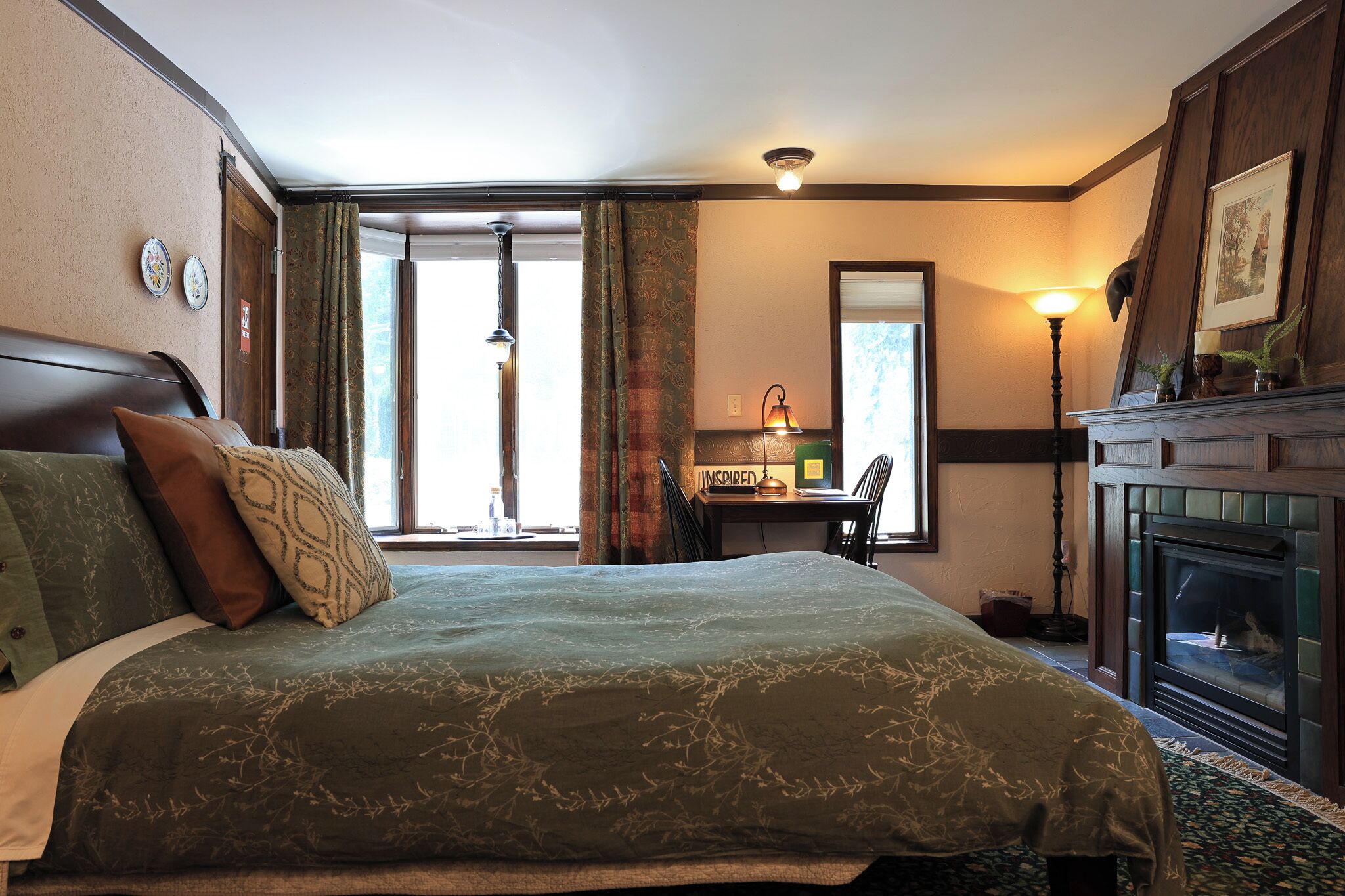 A hotel room with a large bed, a desk, a fireplace, and a view of the outdoors.