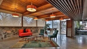 A spacious lobby with a stone wall, a red sofa, green chairs, and a coffee table. - Stone Chalet B&B Inn and Event Center (Ann Arbor)