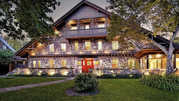 A large, multi-story stone house with a prominent red door, multiple windows, and a balcony. - Stone Chalet B&B Inn and Event Center (Ann Arbor)
