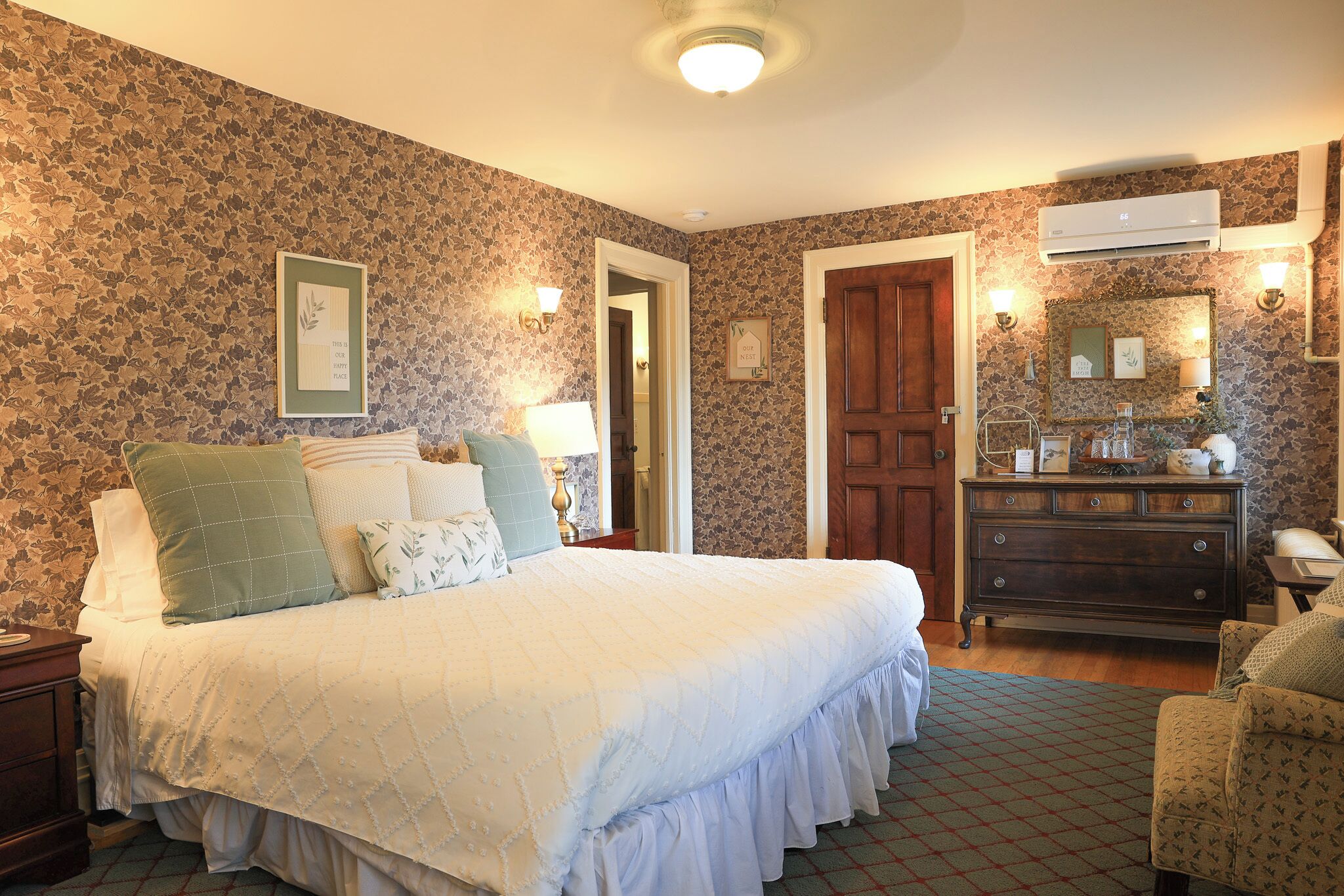 A bedroom with a large bed, a dresser, a mirror, and a door.
