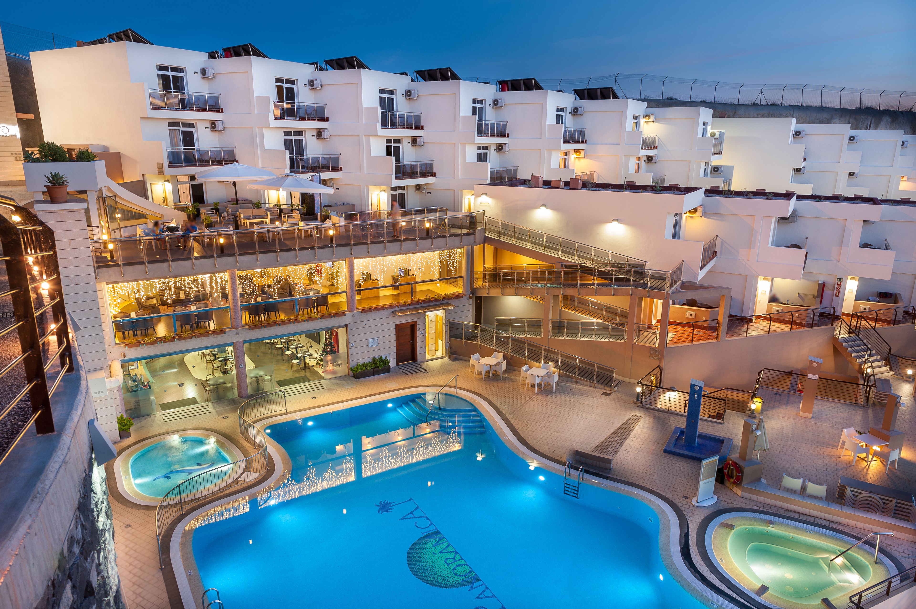 A multi-level hotel with a swimming pool, outdoor seating, and balconies.