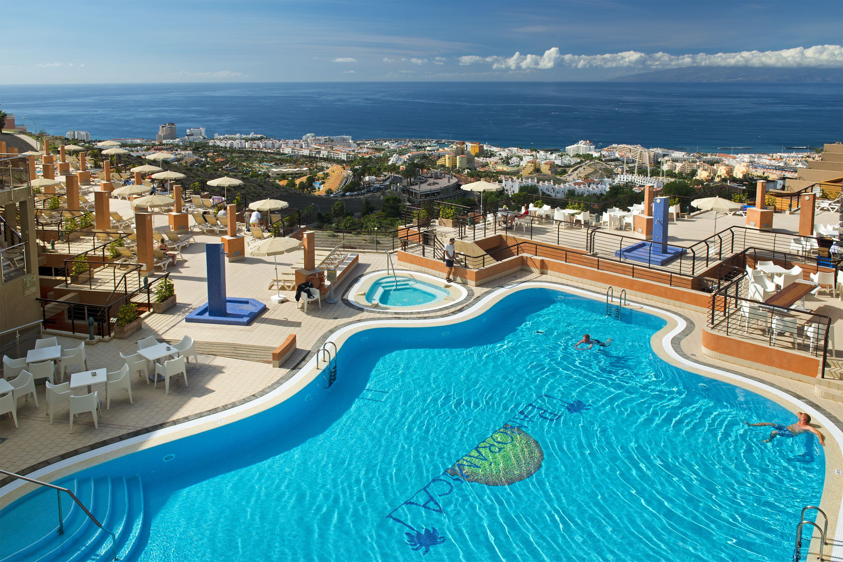 A large outdoor swimming pool with a view of the ocean and cityscape.