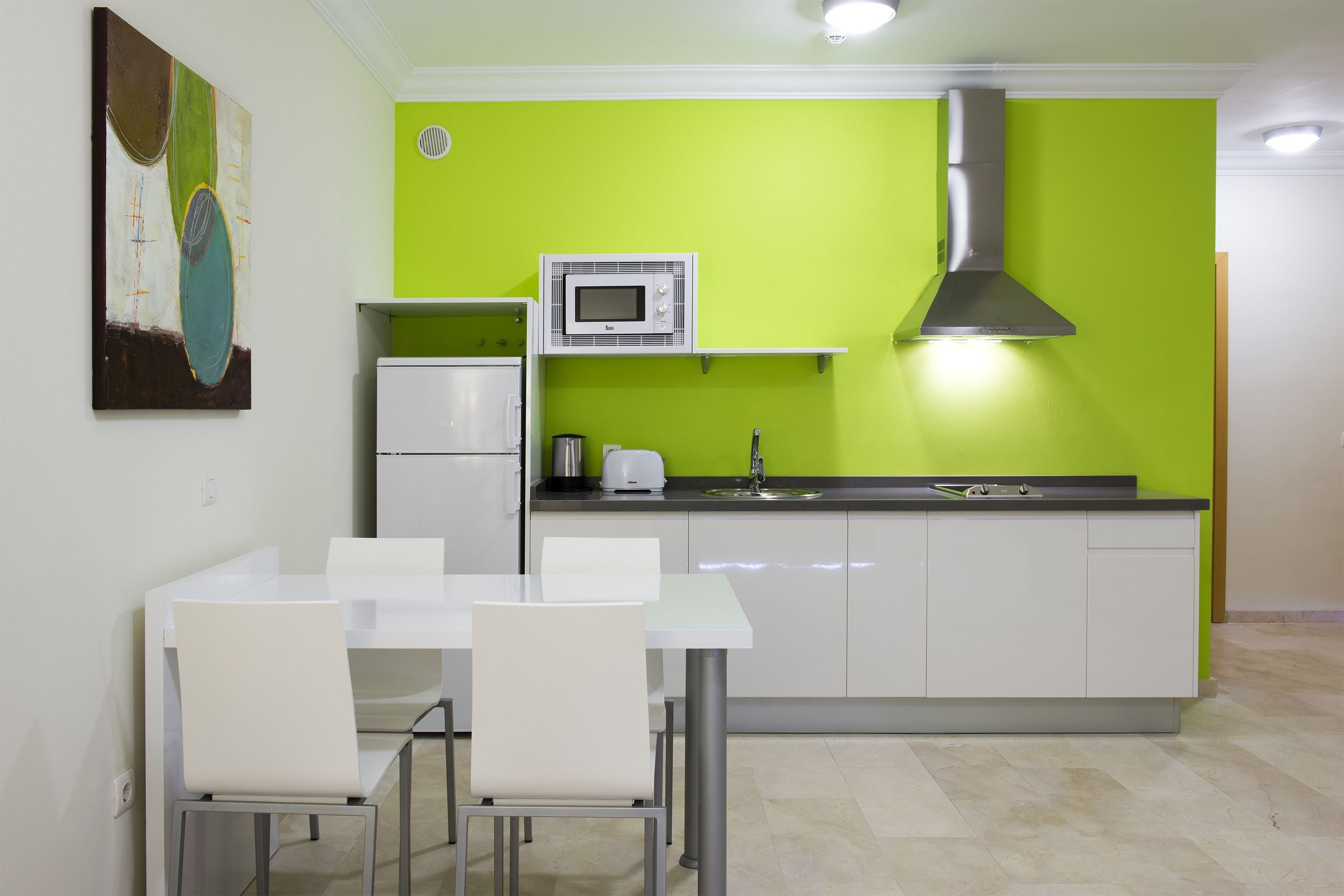 Una cocina moderna con armarios blancos, una pared de acento verde, un microondas y una campana extractora de acero inoxidable.
